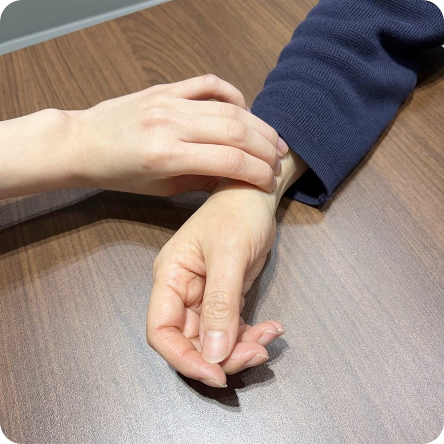 나무 책상 위에 놓인 손목을 다른 손으로 짚어 진맥하는 모습, 남색 니트 소매