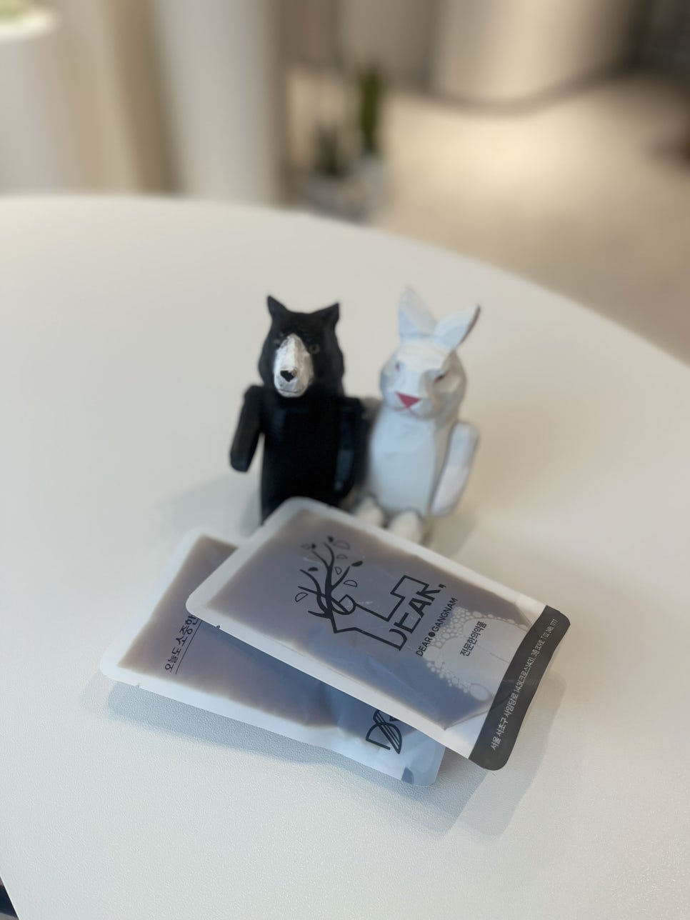Two DEAR herbal medicine pouches on a white table beside two small wooden figures