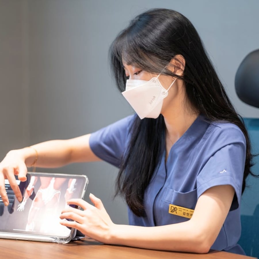 마스크를 쓴 김민지 대표원장이 진료실 책상에서 태블릿 화면을 짚으며 설명하는 모습