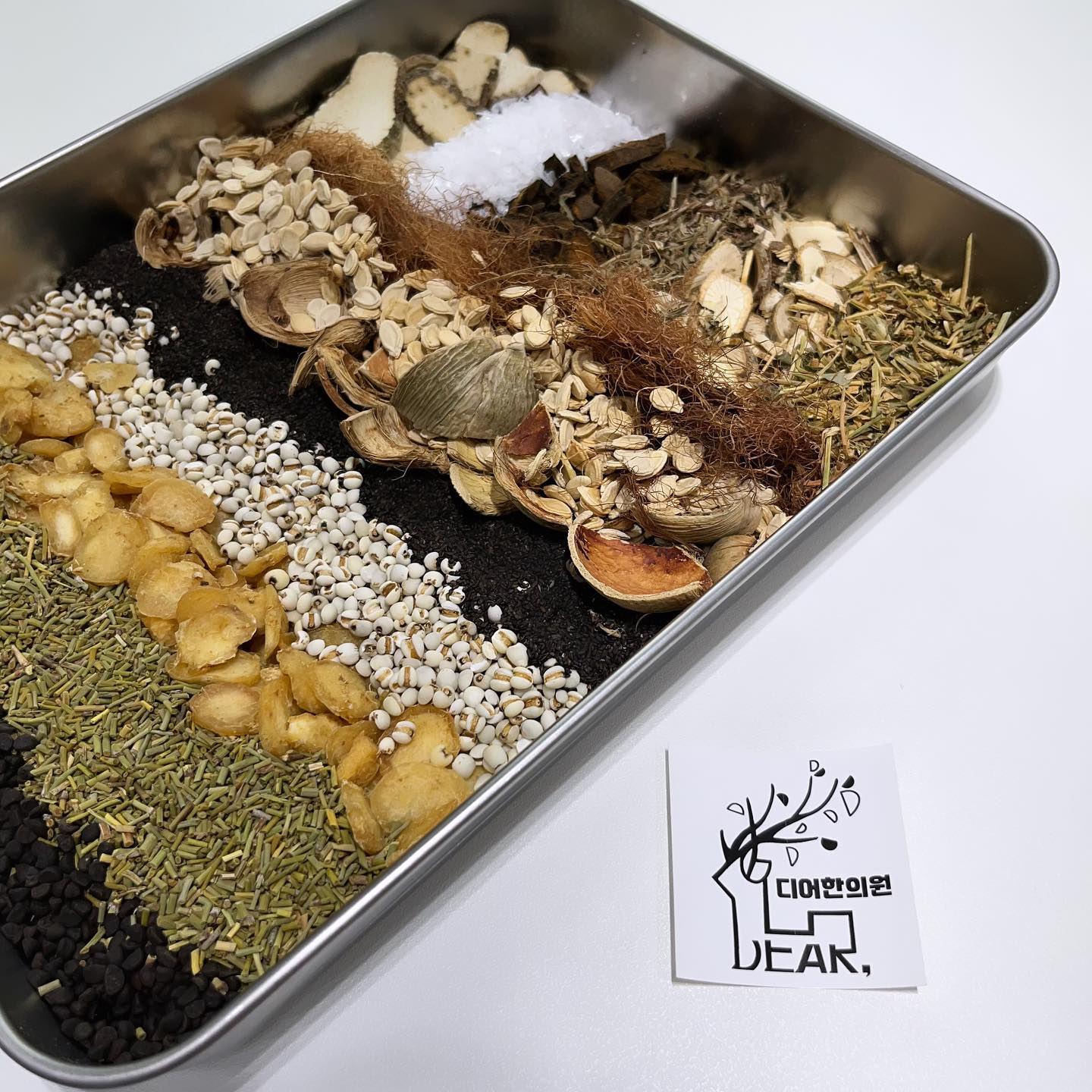 A stainless steel tray of dried herbs laid out in rows beside a DEAR card